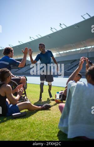 Männliche Amputierte und querschnittsgelähmte Athleten haben im sonnigen Stadion hohe Fiving Stockfoto