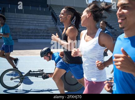 Athleten laufen und im Sportrollstuhl auf sonniger Sportstrecke Stockfoto