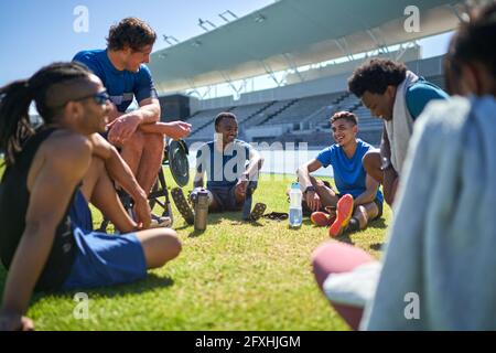 Junge männliche Sportfreunde ruhen sich aus und unterhalten sich auf dem sonnigen Stadionrasen Stockfoto