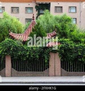 Nur das Dach eines kleinen Tempels ragt aus einem üppigen Garten vor einem Mehrfamilienhaus heraus. Stockfoto