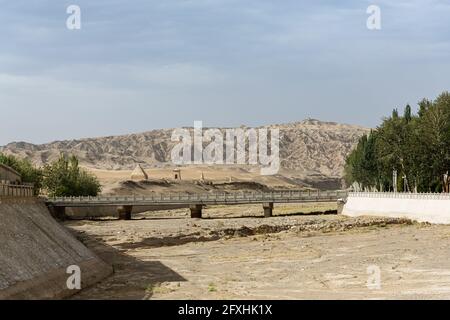 Brücke über einen trockenen Fluss. Kleine Tempel und hohe Sanddünen sind im Hintergrund zu sehen. Stockfoto