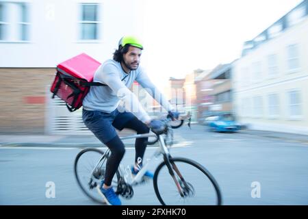 Männlicher Fahrradkurier, der Essen auf dem Fahrrad in der städtischen Nachbarschaft liefert Stockfoto