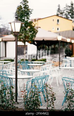Open-Air-Restaurant. Korbstühle und Tische stehen draußen in der Nähe von leuchtenden Laternen vor dem Hintergrund von Häusern Stockfoto