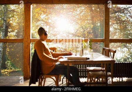 Geschäftsmann mit Kopfhörern, der in einem sonnigen Herbstcafe am Laptop arbeitet Stockfoto