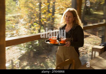 Die Barista trägt Kaffee auf dem Tablett entlang des sonnigen Herbstcafe-Fensters Stockfoto