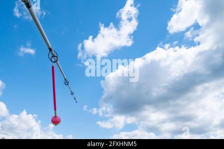 Spinning, Angelrute mit einem hängenden rosa Alarm. Angelausrüstung gegen einen blauen Himmel mit weißen Wolken. Hochwertige Fotos Stockfoto