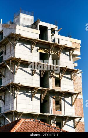 Gerüst an der Fassade eines im Bau befindlichen Mehrfamilienhauses vor dem Hintergrund eines strahlend blauen Himmels. Nahaufnahme Stockfoto