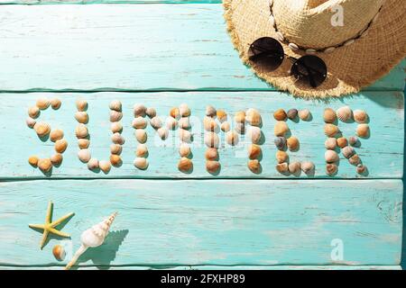 Das Wort Sommer, bestehend aus Muscheln auf einem türkisfarbenen Holzhintergrund, Draufsicht. Stockfoto