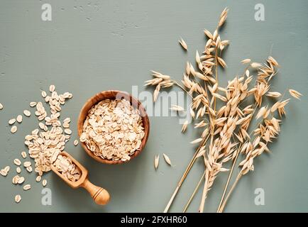 Haferflocken in Holzschüssel und Haferohren auf blauem Hintergrund. Flocken für Haferflocken und Müsli. Stockfoto