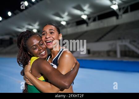 Glückliche weibliche Leichtathleten umarmen sich nachts auf der Strecke Stockfoto