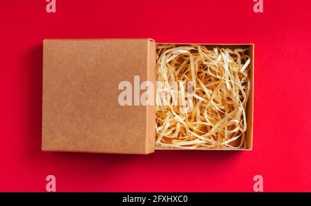 Isoliertes Foto einer Kartonverpackung mit Sägemehl auf rotem Hintergrund. Stockfoto