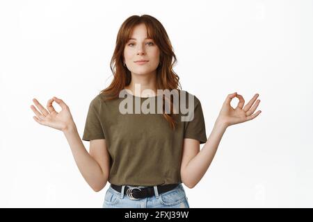 Ruhiges und entspanntes Rotschopf-Mädchen meditierend, Hände seitwärts haltend, Nirvana Zen Pose, Yoga üben, atmen und ausruhen, Über Weiß stehend Stockfoto