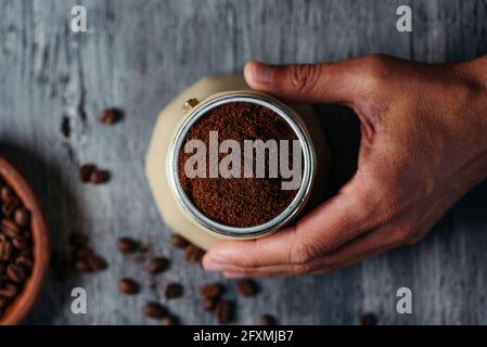 Blick aus der Perspektive eines jungen kaukasischen Mannes, der Kaffee in einer beigen Mokakapfanne an einem grauen rustikalen Holztisch zubereitet Stockfoto