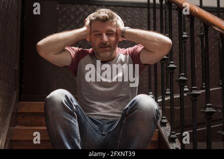 Arbeitslosigkeit und Scheidung - dramatische Lifestyle-Porträt der traurigen und Deprimierter Mann in den 40er Jahren, der im Haus auf der Treppe saß, nachdenklich Und besorgt sufferi Stockfoto