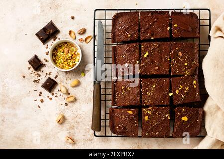 Schokoladenquadrate mit Pistazien und Erdbeeren auf einem Metallständer auf einem hellen Steingrund, Draufsicht, horizontale Komposition. Flach liegend Stockfoto