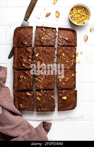 Schokoladenquadrate mit Pistazien und Erdbeeren auf weißem Papier auf hellem Hintergrund, Draufsicht, horizontale Komposition. Flache Lebensmittel Stockfoto