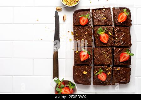 Schokoladenquadrate mit Pistazien und Erdbeeren auf weißem Papier auf hellem Hintergrund, Draufsicht, horizontale Komposition. Flache Lebensmittel Stockfoto