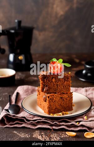 Stapel von Stücken oder Tafel Schokolade Kuchen Brownie mit Erdbeeren und Pistazien Nüsse auf dem schwarzen Hintergrund, selektive Fokus Bild Stockfoto