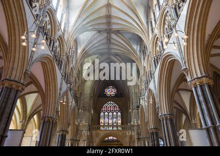 Blick entlang des sonnendurchfluteten Kirchenschiffs zum farbenfrohen Buntglasfenster Great West Window der Lincoln Cathedral, Lincoln, Lincolnshire, England, Vereinigtes Königreich, Europa Stockfoto