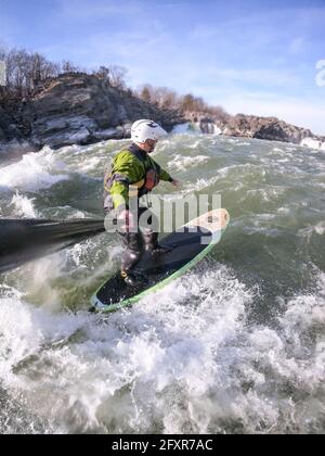 Der Fotograf Skip Brown steht im Winter auf Paddle und fordert Wildwasser unter den Great Falls des Potomac River, USA Stockfoto