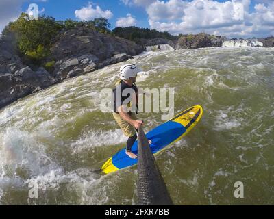 Skip Brown surft auf seinem Stand Up Paddleboard in schnellem Wildwasser am Potomac River in der Nähe von Great Falls, Virginia, USA, Nordamerika Stockfoto