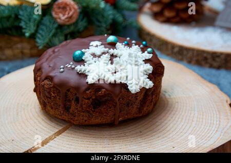 Winterurlaub Cupcake. Weihnachtskuchen aus dunklem Keks mit Schokoladenvereisung. Der Kuchen ist mit Schneeflocken bemalt, das Kambium liegt auf einem Holzboden Stockfoto