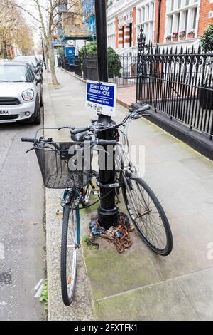 Fahrräder, die an die Straße gekettet waren, mit einem Schild, Kensington, London, Großbritannien,, wo man keinen Müll abwerfen sollte Stockfoto