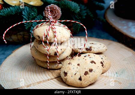 Haferflockenkuchen mit Schokoladenstücken. Ein Stapel von Lebern, die mit einer rot-weißen Kordel vor dem Hintergrund eines Weihnachtsbaums gebunden sind Stockfoto