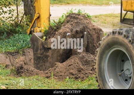 Ein Eimer eines Bulldozers gräbt den Boden mit einem Gras Nahaufnahme in einem Industriegebiet. Aushubarbeiten auf der Baustelle. Stockfoto