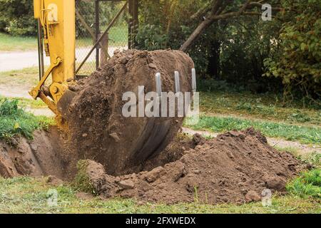 Ein Eimer eines Bulldozers mit einem Haufen Land neben einer Grube in einem Industriegebiet. Aushubarbeiten. Stockfoto