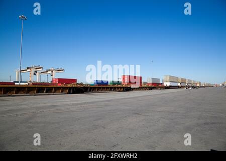 Eisenbahnhof mit Containern, die mit Pritschenwagen auf den Zug geladen wurden Mit Kran im Hintergrund Stockfoto