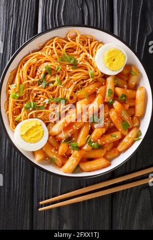 Beliebte koreanische Snack-Mahlzeit in Rabokki geht es um würzige Reiskuchen und Ramen-Nudeln aus der Nähe in der Schüssel auf dem Tisch. Vertikale Draufsicht von oben Stockfoto