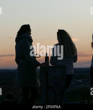 Sillhouettes von 2 Freunden verbringen ihre Nacharbeitszeit mit einem Drink auf einem städtischen Berg. Stockfoto