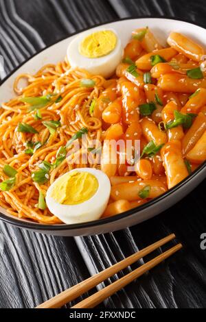 Beliebte koreanische Snack-Mahlzeit in Rabokki geht es um würzige Reiskuchen und Ramen-Nudeln aus der Nähe in der Schüssel auf dem Tisch. Vertikal Stockfoto