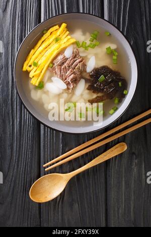 Traditionelles Neujahrsgericht Tteokguk ist eine Suppe, die aus in Scheiben geschnittenen Reiskuchen hergestellt wird, in der Regel in Rinderbrühe, die in der Schüssel auf dem Tisch in der Nähe ist. Vertikale Ansicht von oben Stockfoto