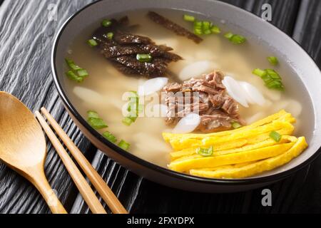 Teeokguk Reiskuchen-Suppe ist eine köstliche, füllende Suppe aus scheibenförmigen Reiskuchen in einer klaren Brühe in der Schüssel auf dem Tisch. Horizontal Stockfoto