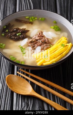 Traditionelles Neujahrsgericht Tteokguk ist eine Suppe, die aus in Scheiben geschnittenen Reiskuchen hergestellt wird, in der Regel in Rinderbrühe, die in der Schüssel auf dem Tisch in der Nähe ist. Vertikal Stockfoto