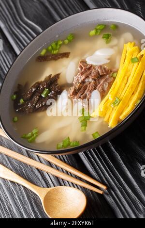 Herzhafte und beruhigende koreanische Reiskuchen-Suppe Tteokguk in der Schüssel auf dem Tisch. Vertikal Stockfoto