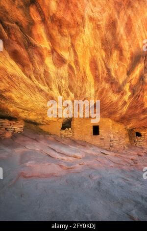 Reflektierendes Sonnenlicht beleuchtet den Sandsteinfelsen oberhalb dieses alten Anasazi Granary und treffend benannt Haus auf Feuerruine in Besuchen Sie Cedar Mesa Pl Stockfoto