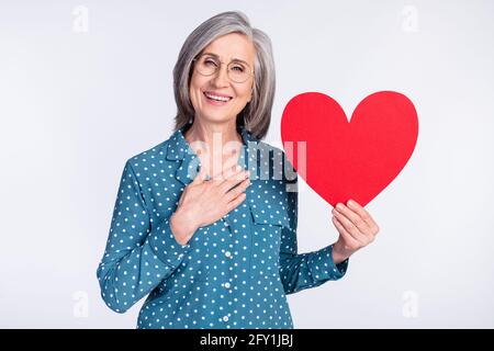 Foto-Porträt einer älteren Dame mit rotem Herz, die die Hand hält Auf der Brust isoliert auf weißem Hintergrund Stockfoto