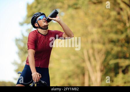 Erschöpfter Straßenradfahrer Trinkwasser aus der Flasche Stockfoto