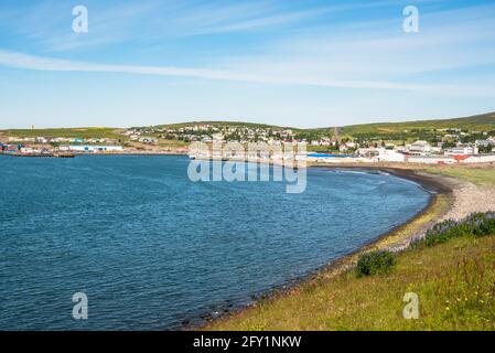 Blick auf eine wunderschöne Küstenstadt mit Häusern am Hang mit Blick auf einen Hafen an einem klaren Sommertag. Im Vordergrund ist ein einsamer Strand zu sehen. Stockfoto