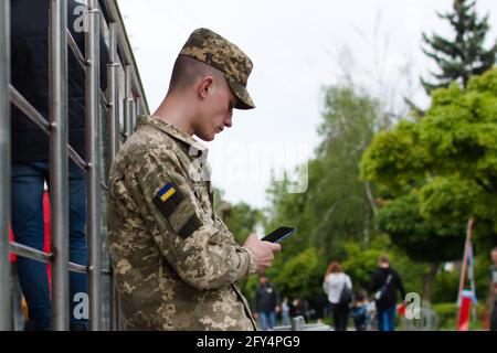 Junger Soldat steht und schaut auf der Stadtstraße in das Smartphone Stockfoto