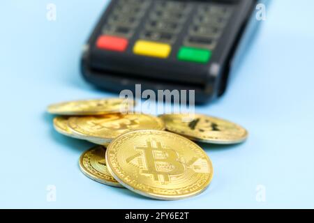 Bitcoin-Münzen in der Nähe des POS-Zahlungsterminals auf dem blauen Hintergrund. Krypto-Währung für die Zahlung Stockfoto
