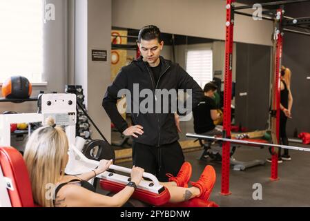 Ein persönlicher Trainer gibt Anweisungen und hilft einer Frau, ihre Beinmuskeln im Fitnessstudio aufzubauen. Sport treiben, Ihren Körper verbessern. Stockfoto