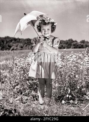 1940ER-JAHRE LÄCHELNDES MÄDCHEN UNTER DEM SONNENSCHIRM, DAS IM FELD STEHT GÄNSEBLÜMCHEN TRAGEN GESTREIFTES KLEID BLUMEN IN IHR HAAR BLICK AUF KAMERA - J1894 HAR001 HARS JOY LIFESTYLE ZUFRIEDENHEIT WEIBCHEN GESTREIFT LÄNDLICHE GESUNDHEIT NATUR KOPIEREN RAUM VOLLER LÄNGE SONNIGEN SCHATTEN B&W DAISY SOMMERZEIT BLICKKONTAKT GÄNSEBLÜMCHEN TRÄUME GLÜCK FRÖHLICH SONNENSCHIRM LÄCHELT FRÖHLICH STILVOLLE WACHSTUM JUGENDLICHE SAISON SCHWARZ UND WEISS KAUKASISCHEN ETHNIE HAR001 ALTMODISCH Stockfoto