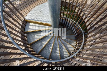 Draufsicht auf eine zauberhafte Wendeltreppe aus Metall in einer von der Sonne beleuchteten Holzkonstruktion. Stockfoto