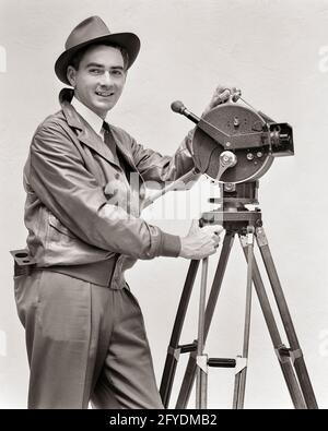 LÄCHELNDER MANN AUS DEN 1930ER JAHREN, KAMERAMANN, DER DIE HANDKURBEL-FILMKAMERA AKELEY BEDIENTE BLICK AUF DIE KAMERA TRÄGT LEDERJACKE FEDORA HUT - U153 HAR001 HARS KARRIERE TECHNOLOGIE INFORMATIONEN FREUDE LIFESTYLE JOBS STUDIO SHOT MOTION DREHARBEITEN KOPIEREN RAUM HALBE LÄNGE PERSONEN INSPIRATION MÄNNER KAMERAMANN BERUF VERTRAUEN TRAGBARE STATIV B & W AUGENKONTAKT KURBEL FEDORA GESCHICKLICHKEIT BERUF GLÜCK FÄHIGKEITEN BETRIEB FRÖHLICH ABENTEUER STRATEGIE KARRIERE WAHL WISSEN RICHTUNG ARBEITERSTOLZ AUF AUTORITÄT BESCHÄFTIGUNG BERUFE LÄCHELT VERBINDUNG KONZEPTUELL IMAGINATION FREUDVOLLE STILVOLLE MITARBEITERJACKE AUS LEDER Stockfoto