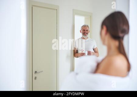 Bärtiger Erwachsener mit Becher und Getränk in der Hand Stehend in der Wohnung Stockfoto