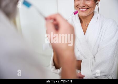 Elegante Frau im weißen Bademantel putzt ihre Zähne im Badezimmer Stockfoto